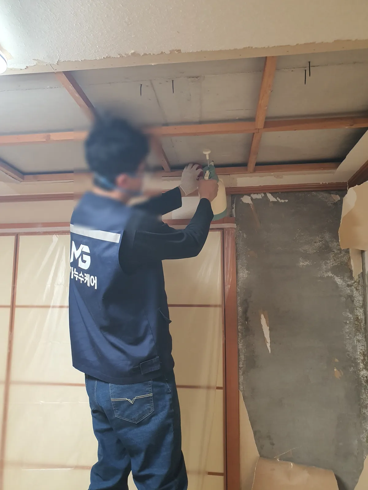 천장 가장자리를 열어 나무 틀이 보이고, 오른쪽 모서리 벽은 벽지가 벗겨져 회색 시멘트에 검은 얼룩이 넓게 남은 모습
