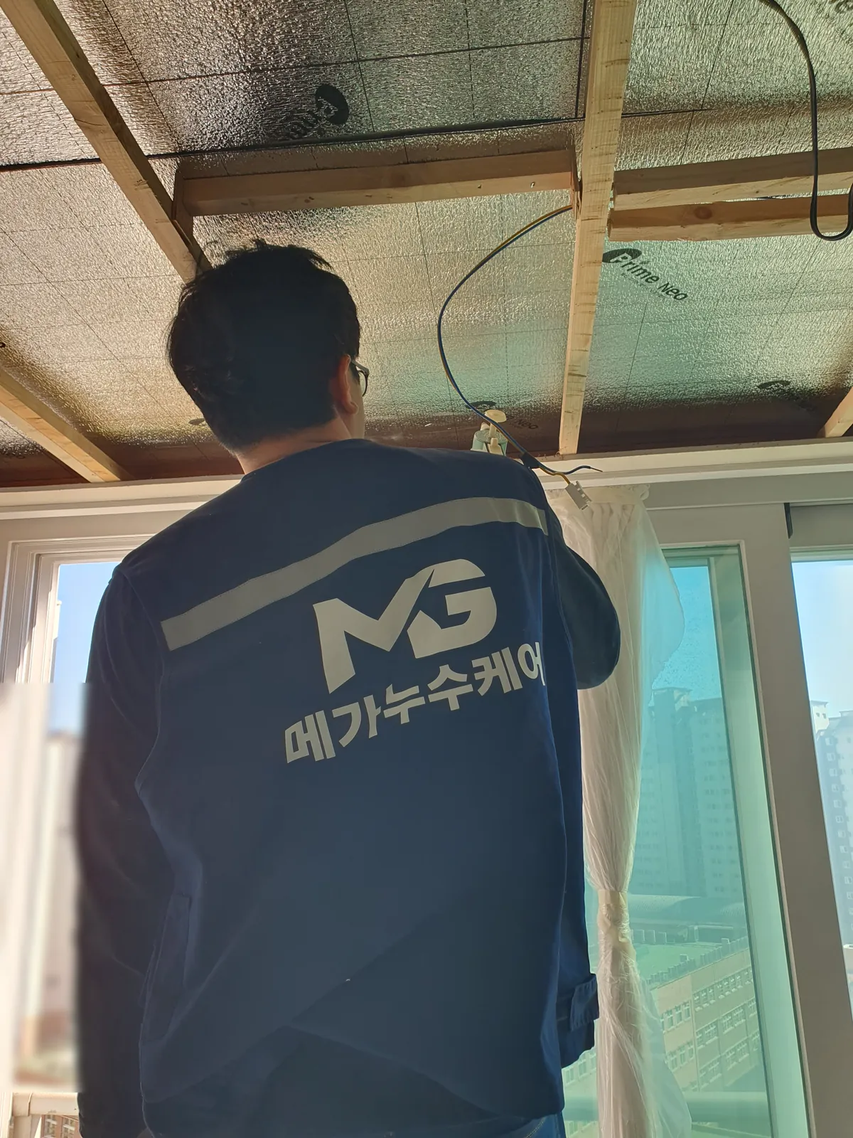 창가 천장 판을 걷어 내 나무 틀과 은박 단열재가 드러난 거실 천장 아래의 작업자 뒷모습
